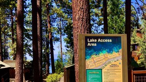 Un panneau d’information dans une zone boisée, indiquant un plan et les règles d’accès au lac.