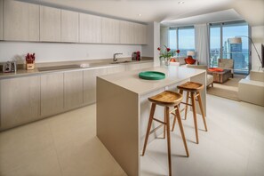 A modern kitchen with a central island, wooden stools, and a view of the city. - BeachFrontResort@Hyde CornerUnit OceanView (Hollywood)