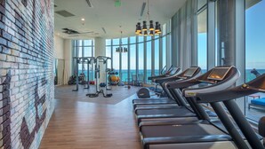 A gym with treadmills, weights, and exercise balls, large windows with a view of the sea, and a brick wall. - Luxurios 2B/2B Condo Beachfront Building (Hollywood)