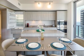 A modern kitchen with a central island, built-in appliances, and a dining area set for four with a vase of flowers. - Luxurios 2B/2B Condo Beachfront Building (Hollywood)