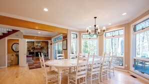 A spacious dining area with a large table and multiple chairs, a chandelier, and large windows offering views of the outdoors. - Luxury Lakefront Gem w/ Hot Tub & Serenity (Oakland)