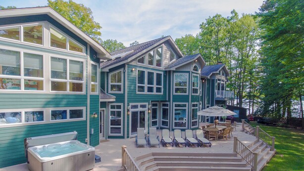 A large house with a hot tub, outdoor seating, and a deck. - Luxury Lakefront Gem w/ Hot Tub & Serenity (Oakland)
