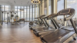 Un gimnasio moderno con cintas de correr, máquinas de pesas y un amplio ventanal con vistas al cielo.