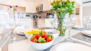 A dining table set with white plates, bowls of fruit, and a vase of white roses. - Cozy designer condo across from the beach. WiFi, parking, tennis and more! (Sunny Isles Beach.)