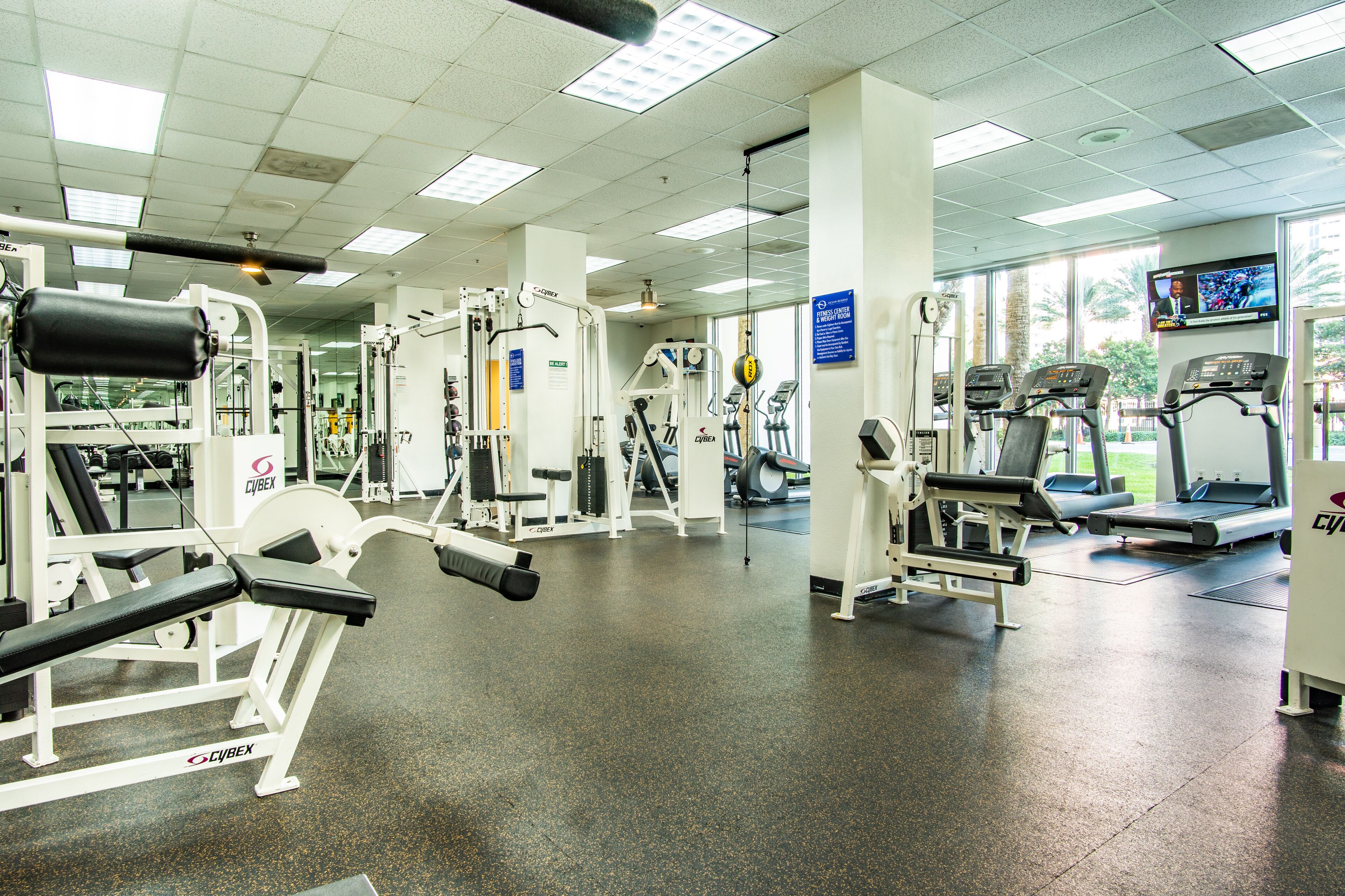 A gym with various exercise equipment, including treadmills and weight machines, under fluorescent lighting.