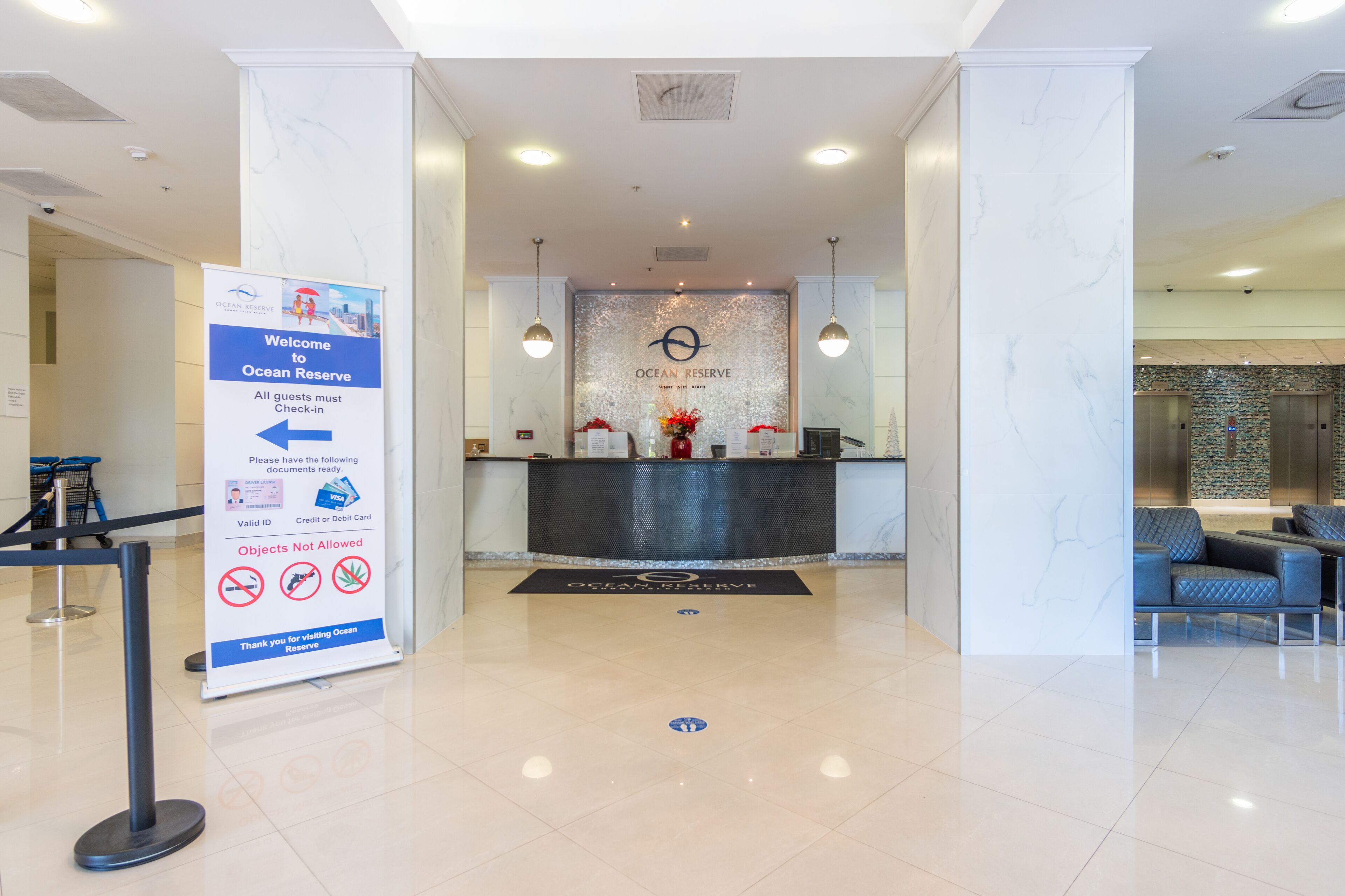 A hotel reception area with a marble floor, a reception desk, and a seating area with blue chairs.