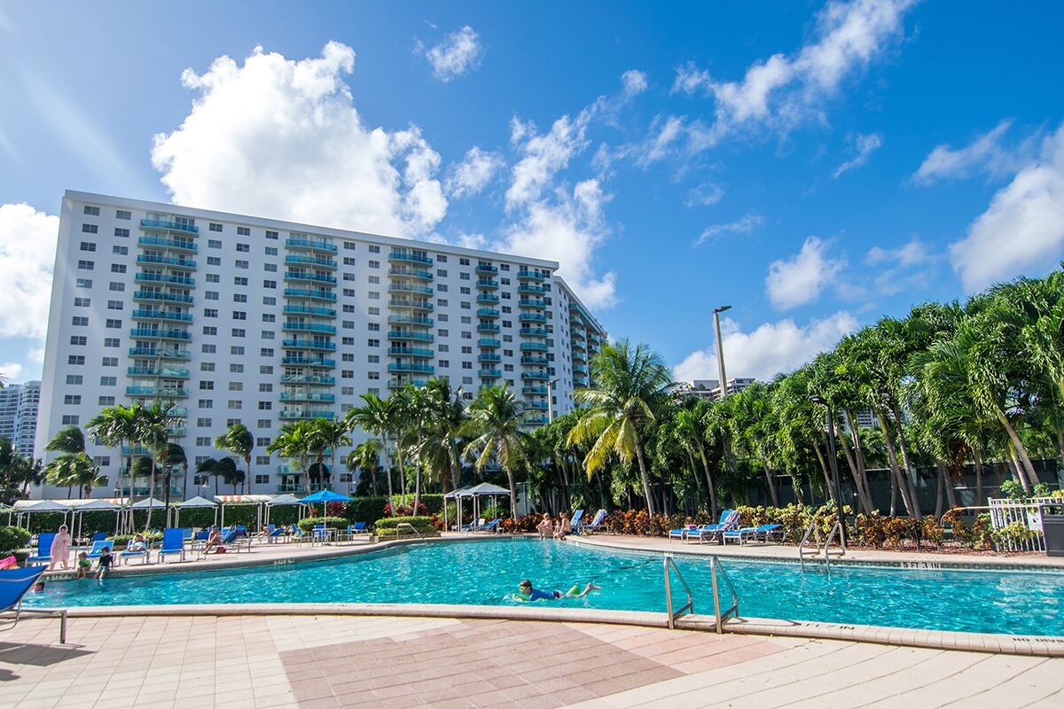 A hotel with a large pool area, palm trees, and a clear blue sky.