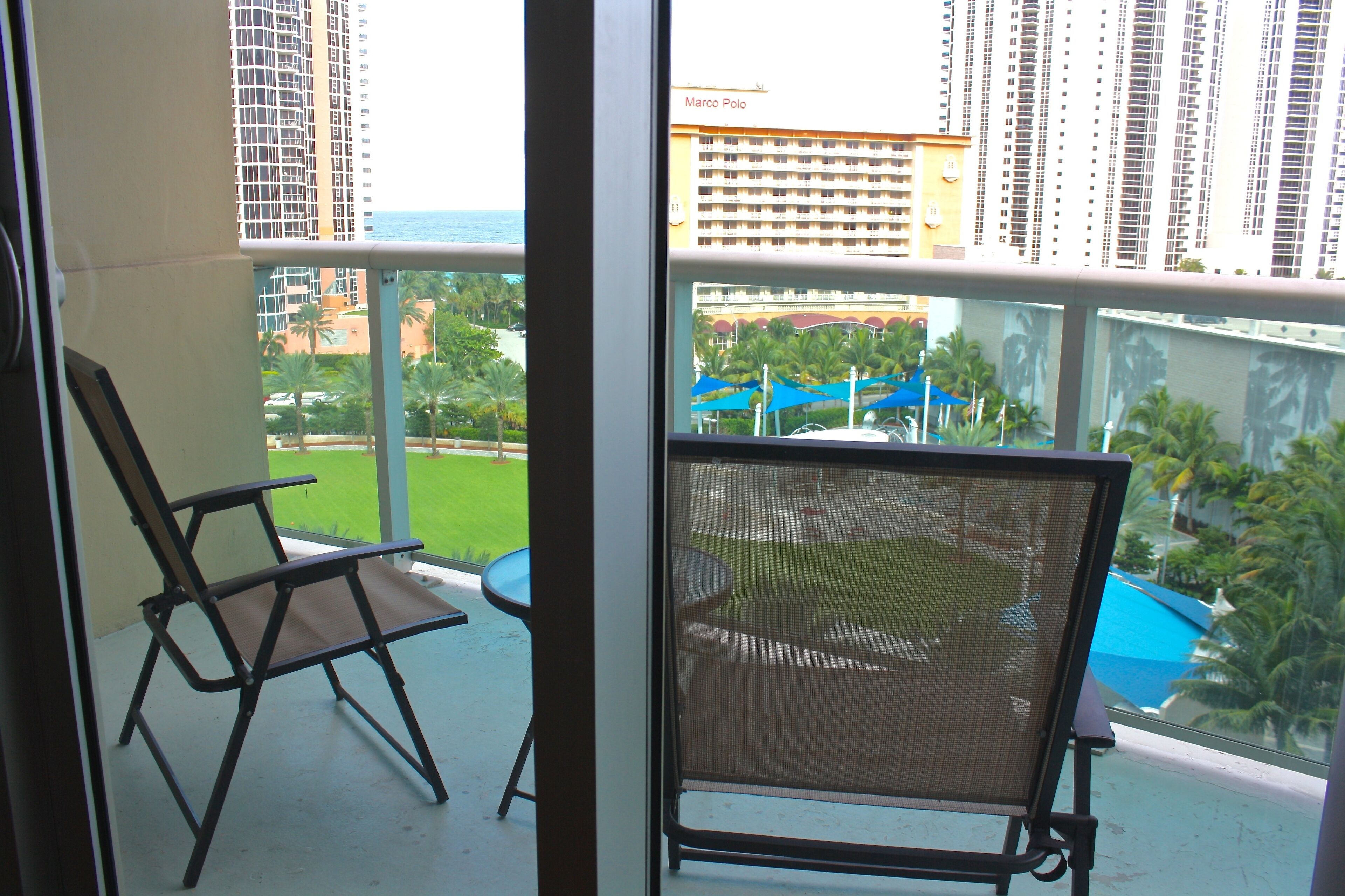 A balcony with two chairs, a view of a pool, and high-rise buildings in the background.