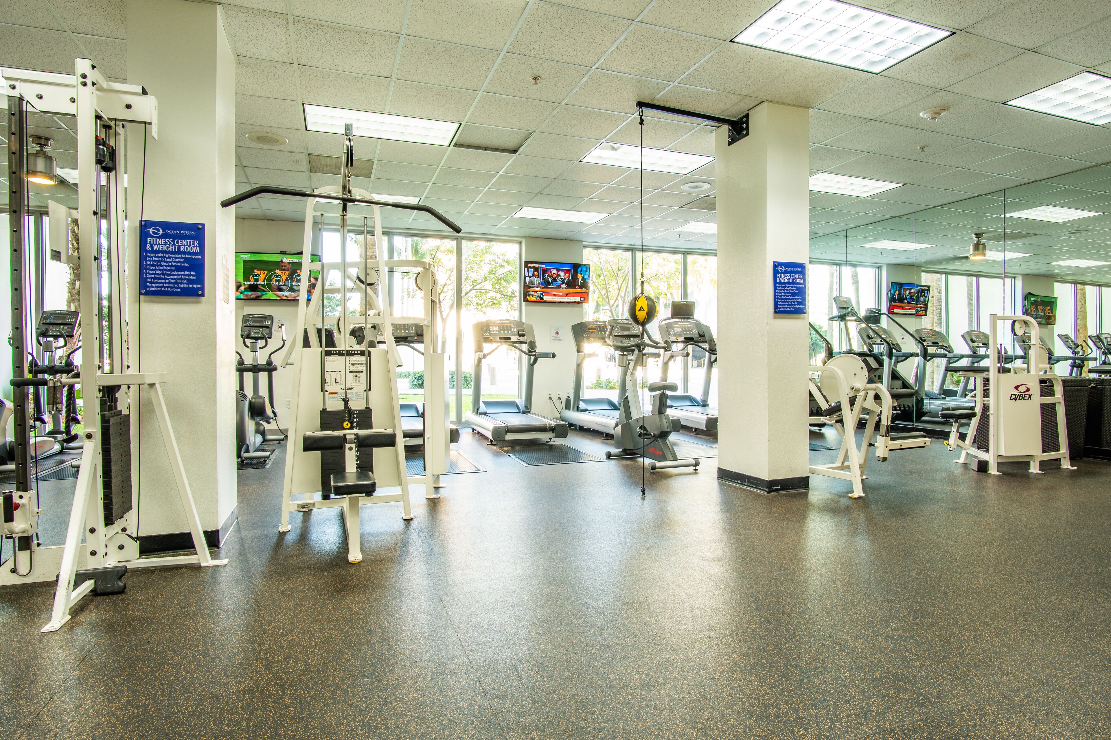 Un centre de remise en forme équipé de divers appareils d’exercice, notamment des tapis de course et des appareils de musculation, et doté d’une grande fenêtre laissant entrer la lumière naturelle.