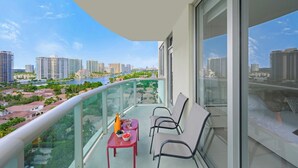 Un balcón con una mesa y sillas, con vistas a un paisaje urbano que incluye edificios y un río.