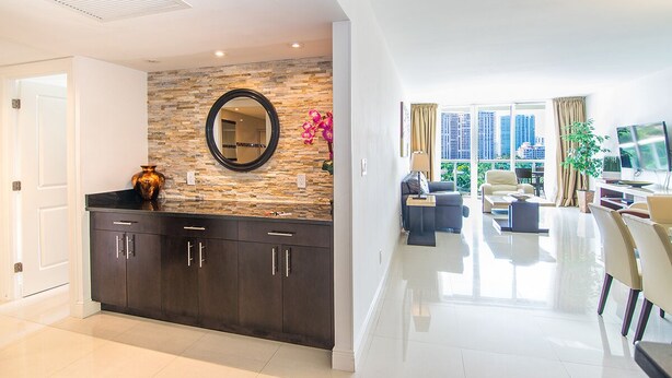 A modern living room with a stone wall, a round mirror, and a large window offering a city view.
