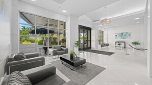 A modern lobby with a seating area, a reception desk, and a large window offering a view of the outdoors. - Modern condo w/ bay views. WiFi, parking, tennis, playground and more! (Sunny Isles Beach.)