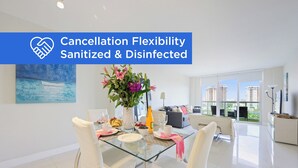 A modern dining area with a glass table, white chairs, and a vase of flowers. - Modern condo w/ bay views. WiFi, parking, tennis, playground and more! (Sunny Isles Beach.)