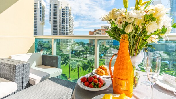 Een balkon met rieten meubels, een tafel met champagne, bloemen, aardbeien en croissants.