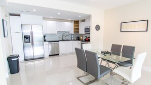 Een moderne keuken met witte kastjes, een roestvrijstalen koelkast en een glazen eettafel met stoelen.