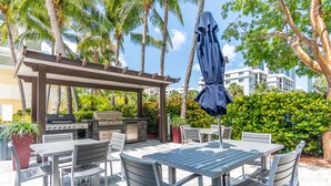 An outdoor patio with a grill, dining table, chairs, and a covered umbrella. - Spacious condo w/ terrace overlooking the bay | WIFI + Parking (Sunny Isles Beach)