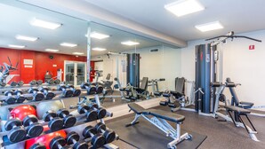 A gym with various exercise equipment, a large mirror, and a red accent wall. - Spacious condo w/ terrace overlooking the bay | WIFI + Parking (Sunny Isles Beach)