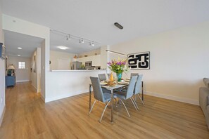 A modern dining area with a table set for four, a kitchen in the background, and a large abstract artwork on the wall. - Spacious condo w/ terrace overlooking the bay | WIFI + Parking (Sunny Isles Beach)
