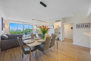 A modern dining area with a table set for four, a sofa, and a view of the outdoors. - Spacious condo w/ terrace overlooking the bay | WIFI + Parking (Sunny Isles Beach)