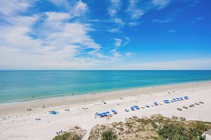 Ein Strand mit klarem, blauem Wasser, sandigem Ufer und blauen Sonnenschirmen.