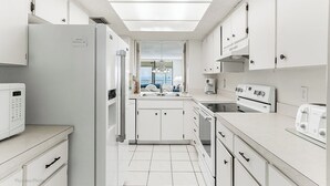 Una cocina moderna con armarios blancos, horno empotrado, microondas y cafetera.