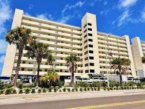 Un hotel de varios pisos con fachada plana, balcones y un estacionamiento con coches.