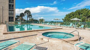 A pool area with lounge chairs, a hot tub, and a building with a balcony. - Reflections 804 - GULF FRONT Condo! (Indian Rocks Beach)