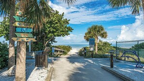 A pathway leading to a beach with palm trees and a fence. - Reflections 804 - GULF FRONT Condo! (Indian Rocks Beach)