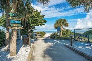 A pathway leading to a beach with palm trees and a fence. - Reflections 804 - GULF FRONT Condo! (Indian Rocks Beach)