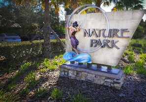A nature park sign with a sculpture of a person climbing a tree.