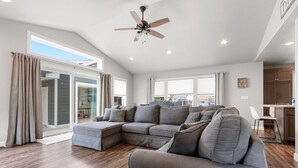 Un soggiorno moderno con un divano componibile, una ventola a soffitto e vista panoramica attraverso ampie finestre.