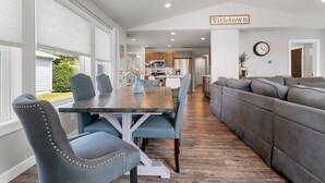 Una cucina moderna con elettrodomestici in acciaio inossidabile, un'area pranzo con tavolo in legno e sedie blu, e un divano grigio nel soggiorno.