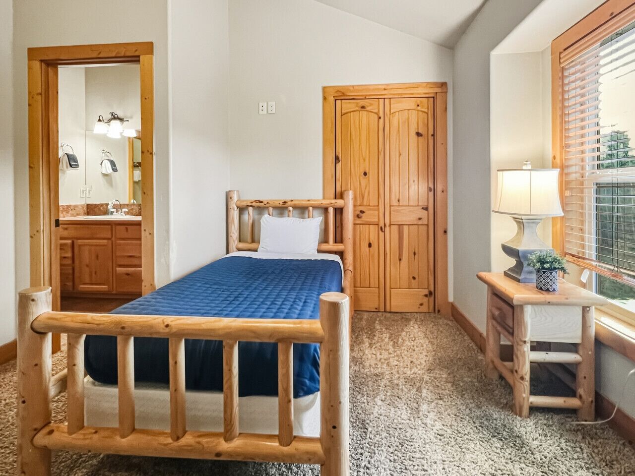 A bedroom with a wooden bed, a small bedside table with a lamp, a mirror, and a wooden wardrobe.