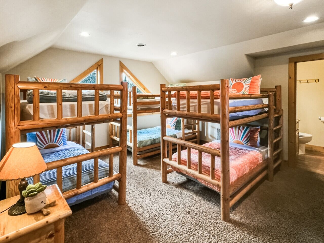 A room with three bunk beds, a small table with a lamp, and a window with a view of trees.