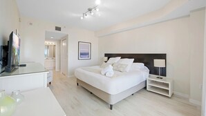 A modern hotel room with a large bed, bedside tables, a TV, and a bathroom visible through an open door. - Comfortable condo with amazing bay views | WIFI + Parking (Sunny Isles Beach)