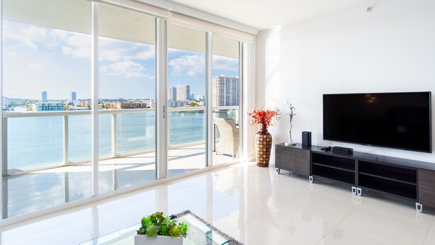 Un soggiorno moderno con una grande TV, un tavolino in vetro e vista sull'acqua e sullo skyline della città.