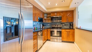 A modern kitchen with stainless steel appliances, wooden cabinets, and a tiled floor. - Warm condo w/ striking ocean & park views | WIFI + Parking (Sunny Isles Beach.)