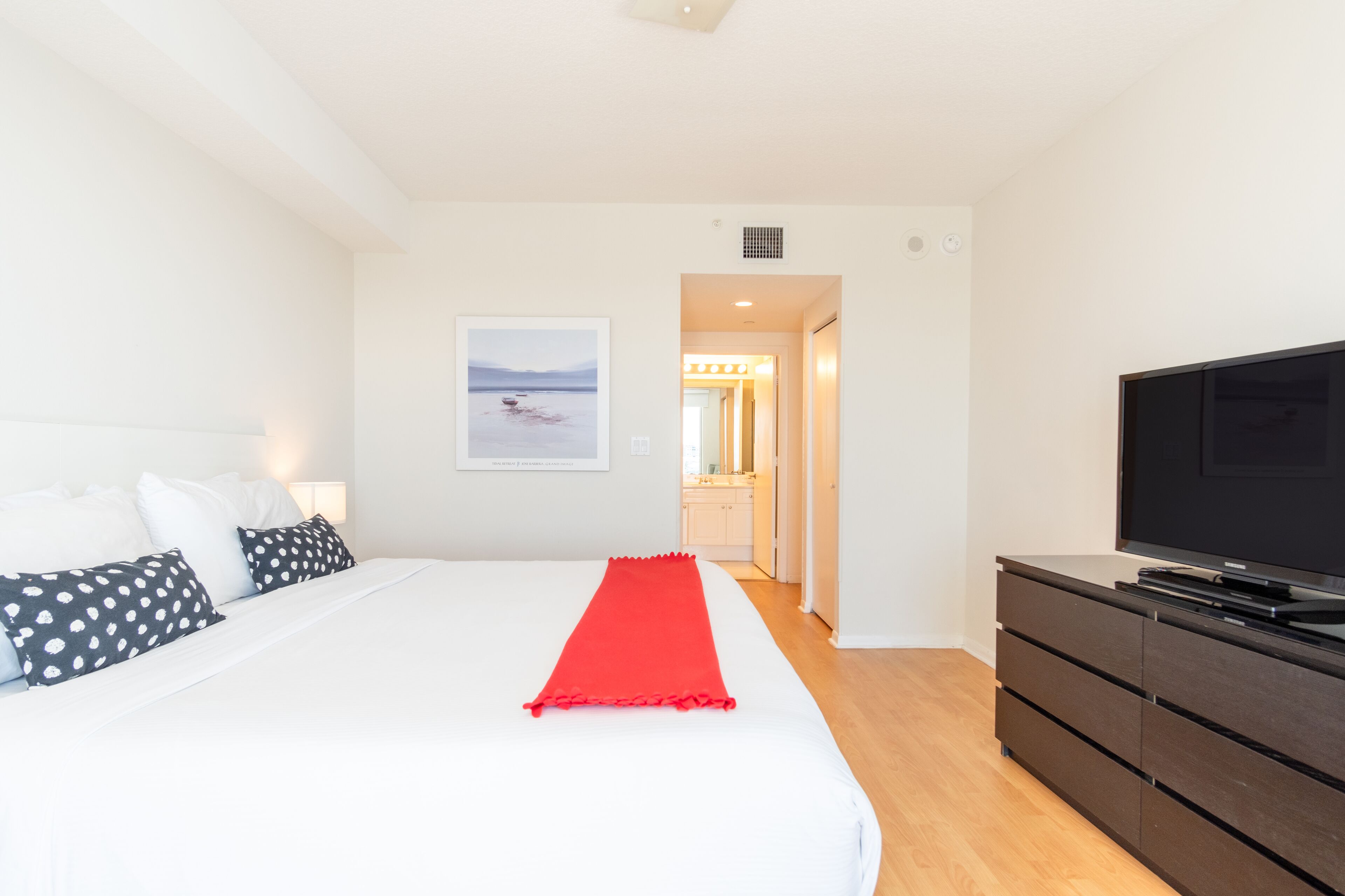 A hotel room with a large bed, a TV, and a red runner.