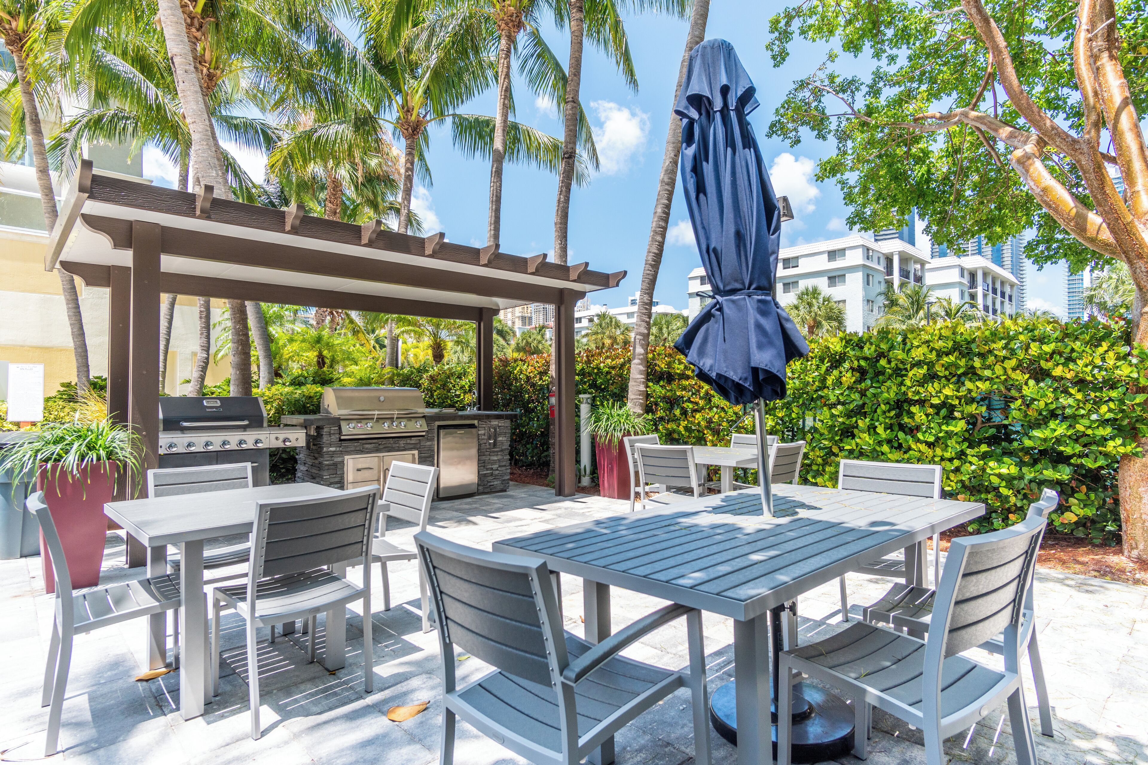 An outdoor patio with a grill, dining table, chairs, and a covered umbrella.