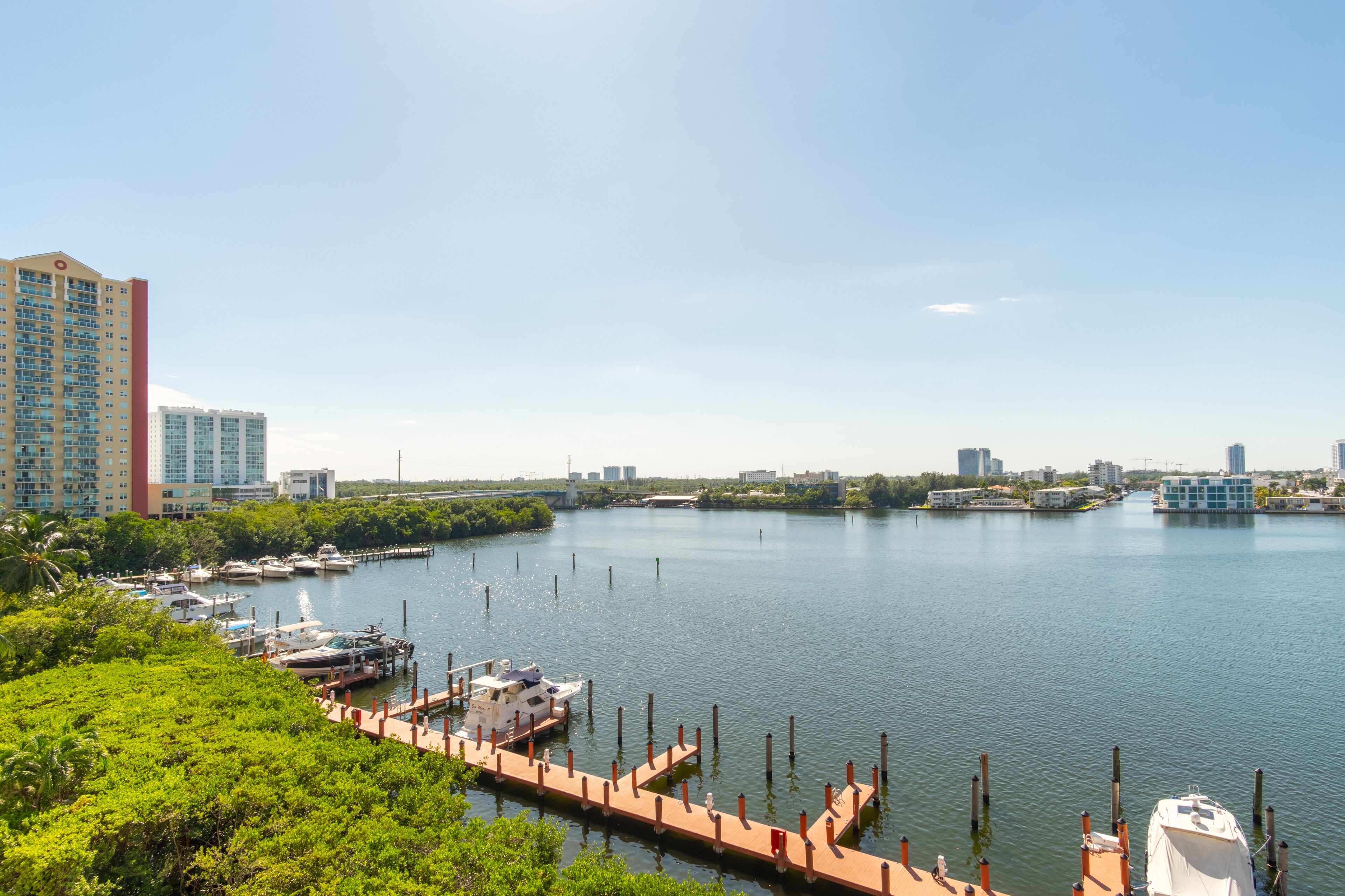 A marina with boats docked, a dock extending into the water, and a city skyline in the background.