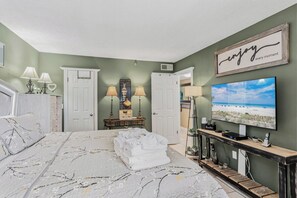 Un dormitorio con cama, televisor, consola y puerta.