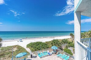 A balcony with a view of a beach, lounge chairs, and a table with umbrellas. - West Coast Vista 2C - GULF FRONT CONDO! (Indian Rocks Beach)