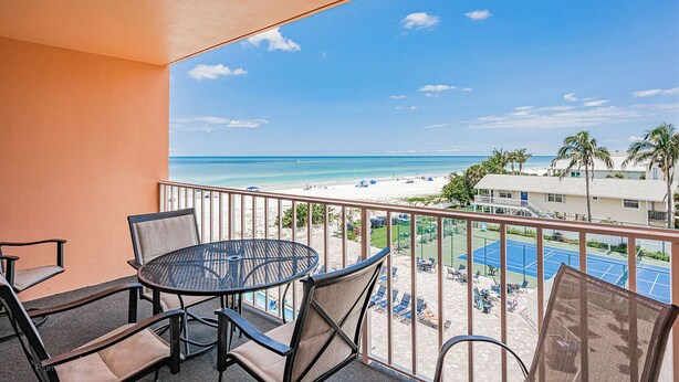 Ein Balkon mit Tisch und Stühlen mit Blick auf Strand und Tennisplätzen.