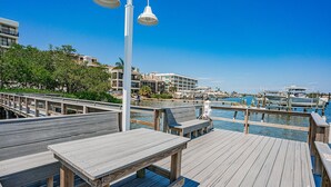 A wooden deck with benches and tables, overlooking a marina with boats and a clear blue sky. - Quiet Waters C1 - INTERCOASTAL VIEW Condo! (Indian Shores)
