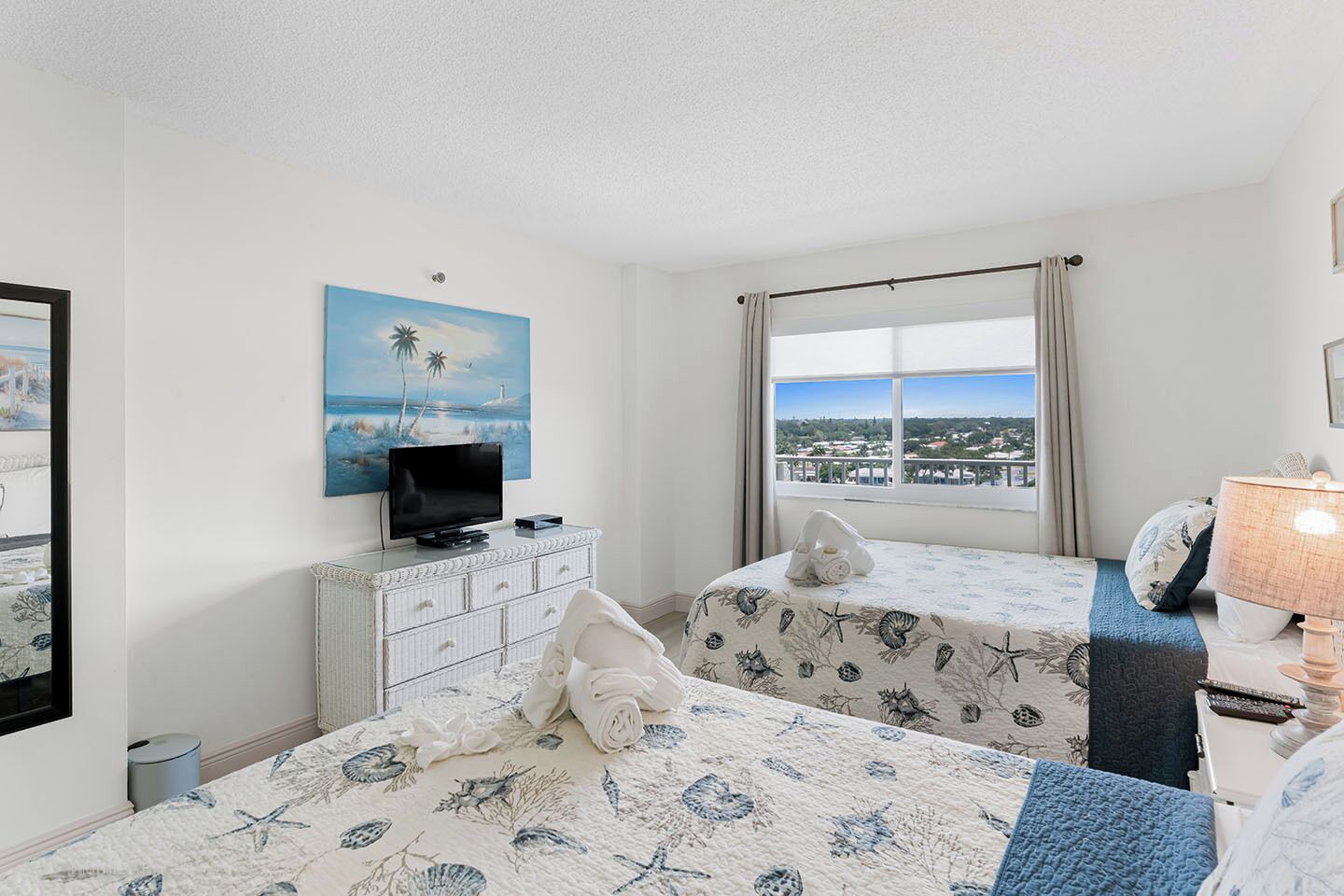 A hotel room with a bed, a TV, a window with a view, and a lamp.