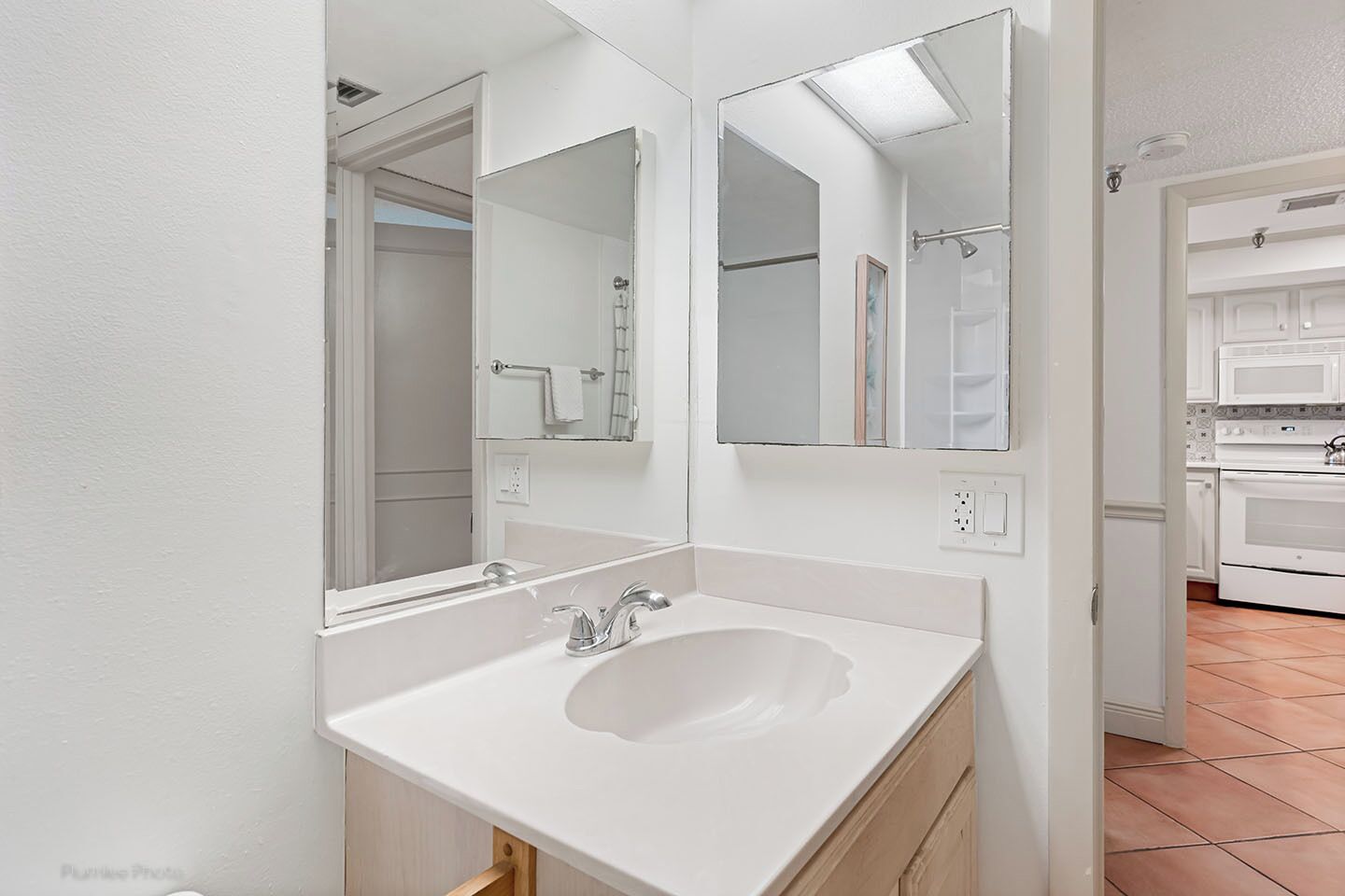 A modern bathroom with a white sink, double mirrors, and a shower area visible through an open door.