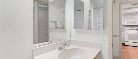 A modern bathroom with a white sink, double mirrors, and a shower area visible through an open door.