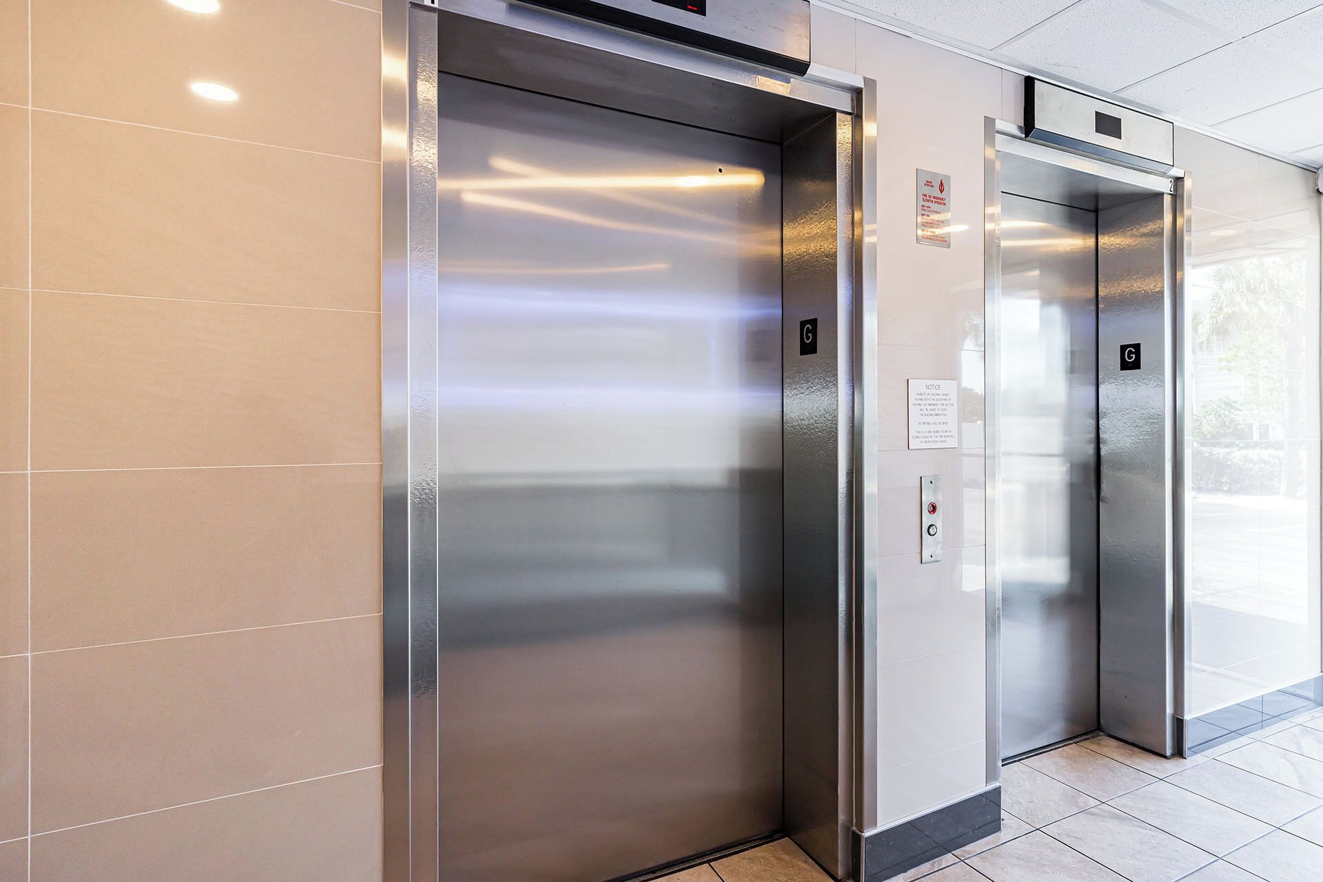 Two elevator doors with a metallic finish, a sign above the right door, and a tiled floor.