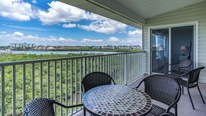 Un balcon donnant sur une rivière et des bâtiments, aménagé avec des fauteuils en osier et une table ronde.