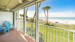 A balcony with a view of the beach, a ceiling fan, and two blue chairs.